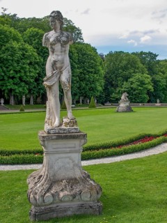 Weathered statue in a well-kept park with green lawns and surrounded by trees, park with green