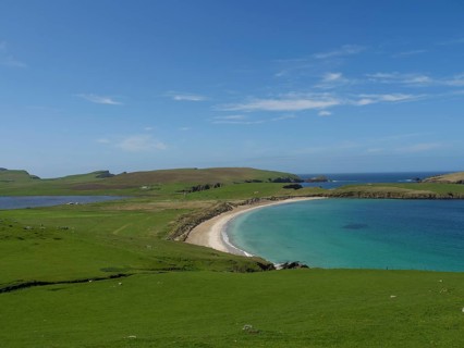 A breathtaking coastal landscape with an elongated beach surrounded by green meadows and clear blue