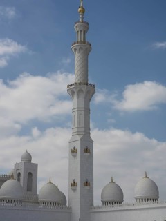 High minaret of a mosque surrounded by white domes and a cloudy sky, large mosque with white domes