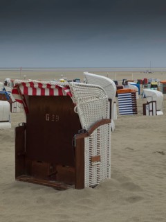 A single beach chair stands on a deserted beach under a cloudy sky, beach chairs and beach tents by