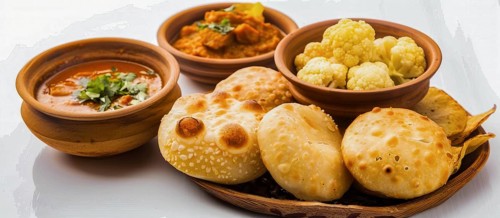 Attractive spread of Indian food with sesame-topped naan, curry, cauliflower, and potatoes in
