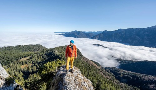 Mountaineer on the rocky summit of the Ettaler Manndl, view over mountain landscape and sea of