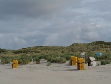 A wide dune landscape with scattered beach chairs under a cloudy sky, colourful beach chairs on the