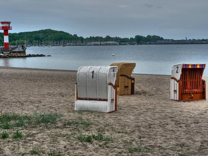 A cloudy day on the beach with a lighthouse in the background and several beach chairs on the sand,