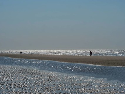 People walking along the beach with reflecting watercourse, glittering sea water at low tide on the