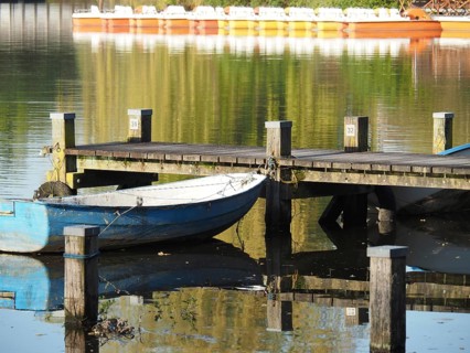 A boat is moored next to a jetty that is reflected in the water, surrounded by peaceful nature,