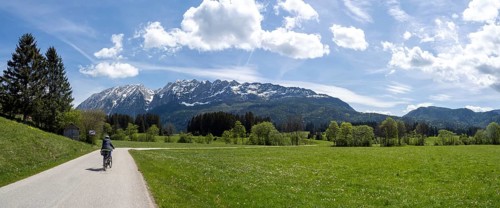 Cyclist on the Ennstal cycle path, path leads through meadows, behind her the Grimming, panoramic