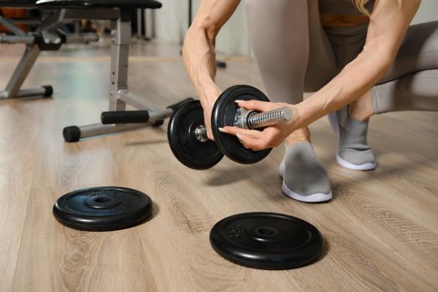 Closeup view of hands of woman adjusting weight on dumbbells in gym