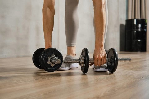 Closeup view of muscular female arms lifting dumbbells from the floor