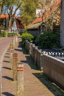 Quiet footpath along a wooden fence, lined with brick houses and trees in a village, historic