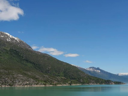 Landscape shot of a lake and forested mountains under a clear blue sky, greenish shimmering water