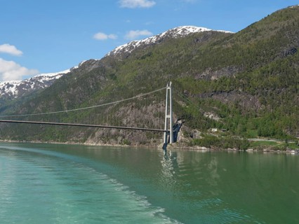 Vast landscape with a bridge stretching over a calm lake and snow-capped mountains under a blue