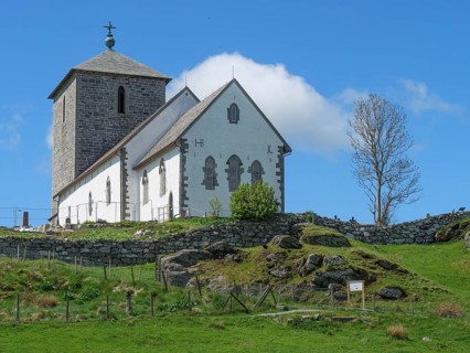 White church with stone tower on a rocky hill under blue sky with clouds, old stone church and many