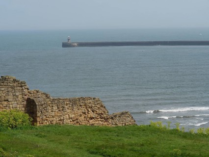 A piece of coastline with ruinous architecture in the foreground and the sea in the background,