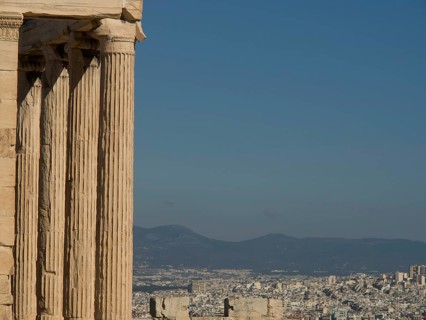 Ancient marble columns with a city and mountains in the background under a clear sky, historical