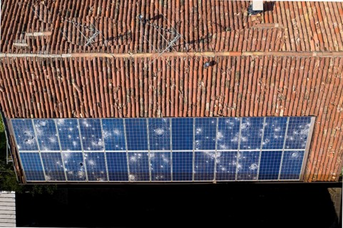 Direct overhead view of a roof with terracotta tiles and damaged solar panels casting shadows