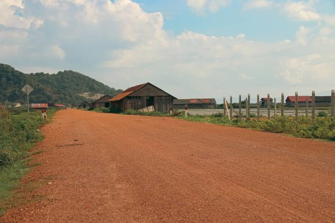 A serene rural landscape with a dirt road leading past wooden salt storage houses and mountains in