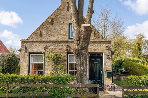 Rustic brick house with tree in the front garden and rural charm, surrounded by green vegetation in