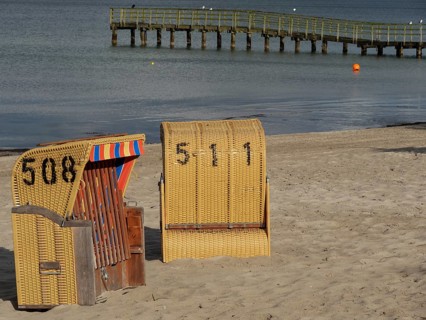 Two beach chairs on the beach near a wooden jetty with calm sea in the background, beach chairs on