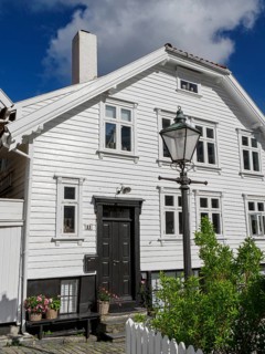 White houses with black doors, flowers and lanterns along a cobblestone street under a blue sky,