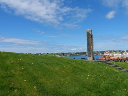 Green meadow with a monument on a hill under a blue sky, old stone church and many gravestones on