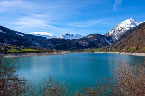 Lake Lungern surrounded by snow-capped mountains and green hills under a blue sky, Lungern,