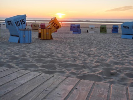 Various beach chairs on a sandy beach during sunset, sea in the background and a wooden walkway in