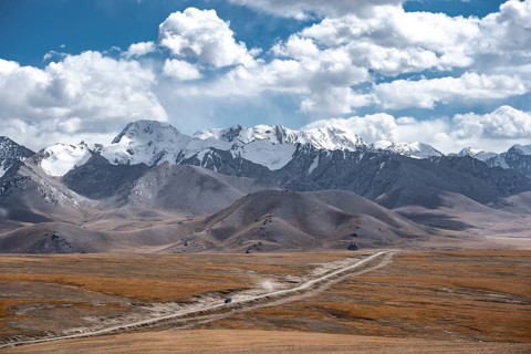 Car on a gravel track in the high mountain plateau, glaciated and snow-covered peaks, Ak Shyrak