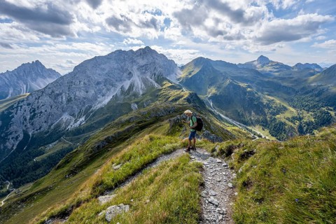 Mountaineer on a hiking trail on a grassy mountain ridge, idyllic mountain landscape with green
