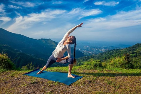 Woman practices yoga asana Utthita Parsvakonasana, extended side angle pose outdoors in mountains