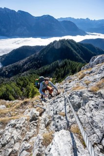 Hiker on via ferrata to Ettaler Manndl, view over mountain landscape and sea of clouds, high fog in