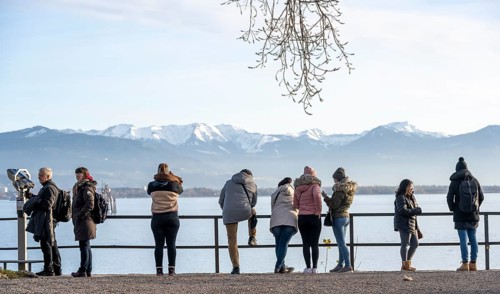 People enjoying the view of snow-covered mountain peaks on Lake Constance in winter, Lindau Island,