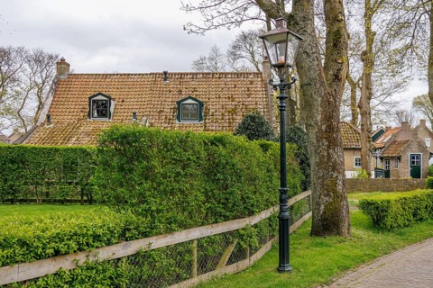 Cosy house in a village, surrounded by green hedges and lanterns, a road leads past, dune and