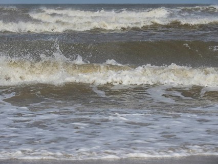 Close-up of churning waves and splashing water in the sea, waves on a beach, sunny day with clouds