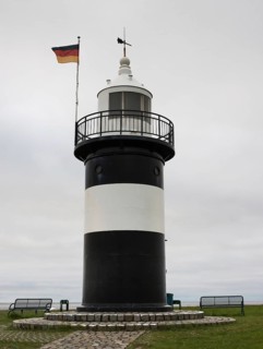 Black and white lighthouse, called 'Kleiner Preusse', at the sea, with German flag, flag waving in