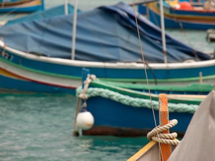 Several boats are quietly moored in the clear waters of a harbour, many colourful fishing boats in