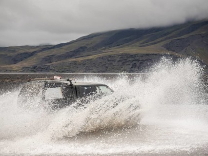 An off-road vehicle quickly crosses a waterway and causes large water fountains in front of a