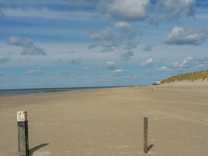 Wide, quiet sandy beach with posts in the foreground under a cloudy sky, clouds on the beach with