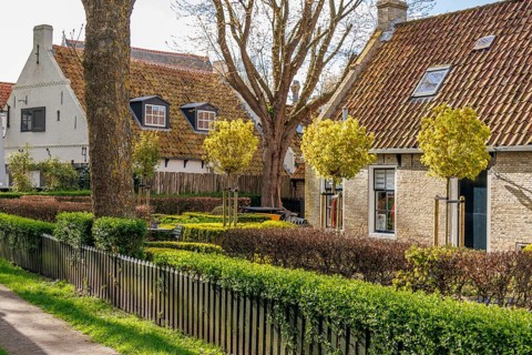 Picturesque village houses with well-tended gardens and green fences under a blue sky, old houses
