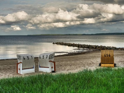 Two white and one yellow beach chair on a sandy beach, rocks in the water and cloudy sky, beach