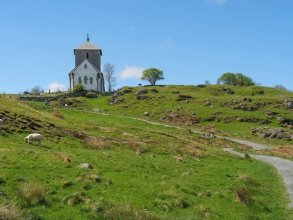 Church on hilly landscape with hiking trail and sheep, blue sky and clouds, old stone church and