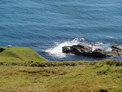 Hilly coastal landscape with grass and rocks sloping down to the blue sea, green meadows on a deep
