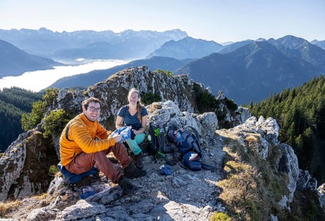 Two hikers at Ettaler Manndl, view over mountain landscape and sea of clouds, high fog in the