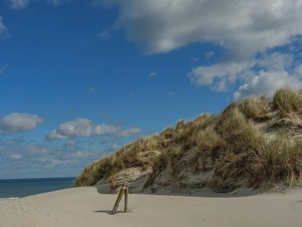 High sand dunes with grass, behind them the sea and a partly cloudy sky, dunes on an island with a