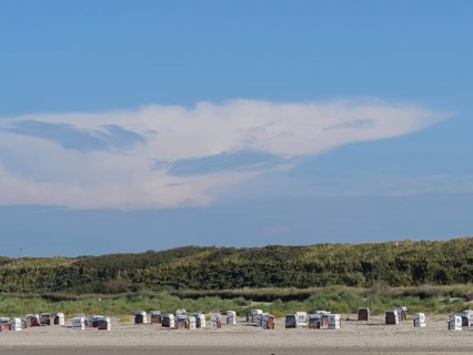 Beach with many beach chairs in front of large dunes, impressive cloud formation in the sky, dunes