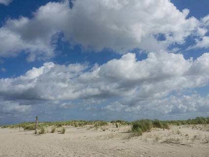 Wide sand dune landscape under a partly cloudy sky, quiet atmosphere, lonely beach with dune grass