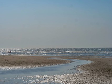 People walking along the beach with a watercourse under a clear blue sky, sparkling sea water at