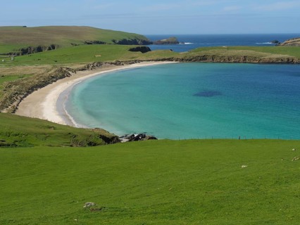 A picturesque stretch of coastline with rolling hills, a golden beach and turquoise waters blending