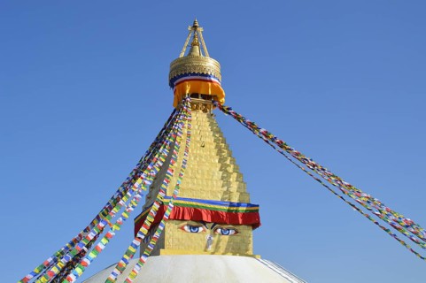 Top part of Boudhanath Stupa or Chaitya adorned with colorful prayer flags under a clear blue sky