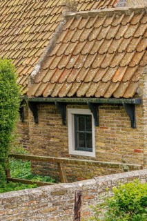 Small brick house with rustic tiled roof and surrounded by fresh green bushes, old houses with